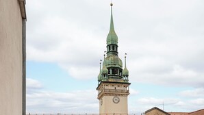 Un balcón con una mesa y dos sillas, una torre del reloj al fondo y un tejado de tejas rojas.