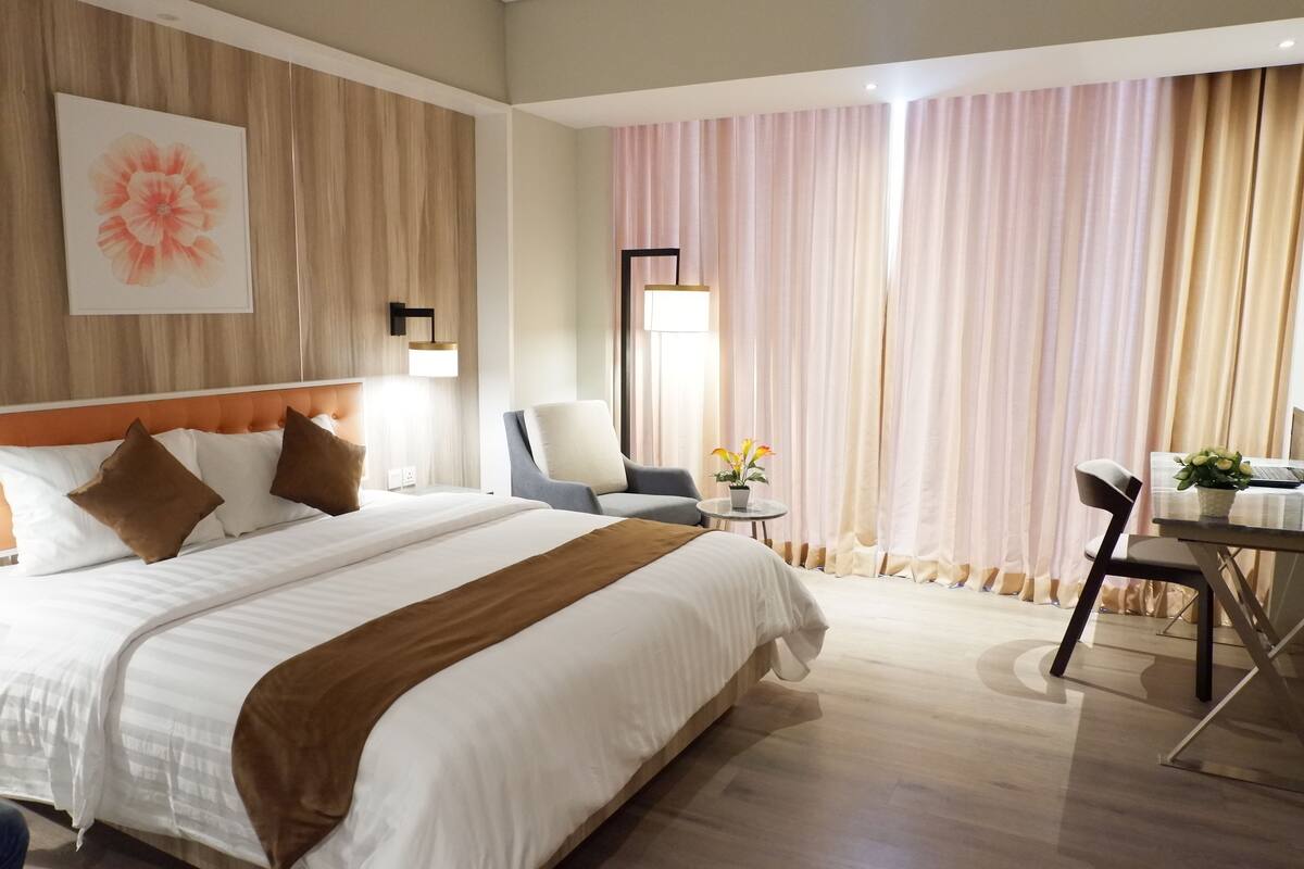 Hotelkamer met een groot bed, een bureau, een stoel en een raam met gordijnen.