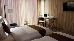 Une chambre d’hôtel avec deux lits, un bureau avec un ordinateur portable, une télévision et une petite table agrémentée de fleurs.