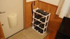 A corner with a white shoe rack holding multiple pairs of shoes, a white candle, and a wooden wall. - Churaumi healing place YURAKUKAN (Motobu)
