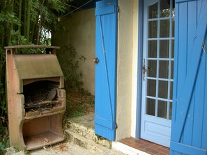 Een robuuste buitenbarbecue met een blauwe deur en een raam, omringd door groen.