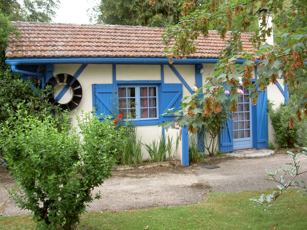 Een traditioneel huis met een pannendak, blauwe luiken en een tuin ervoor.