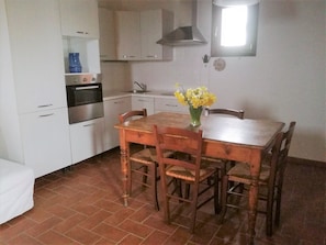 Cozinha compacta com armários brancos, fogão e mesa de jantar com cadeiras.
