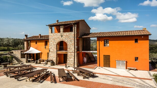 A building with a stone and orange facade, multiple balconies, and outdoor seating areas. - Agriturismo Borgo Stella (Montespertoli)