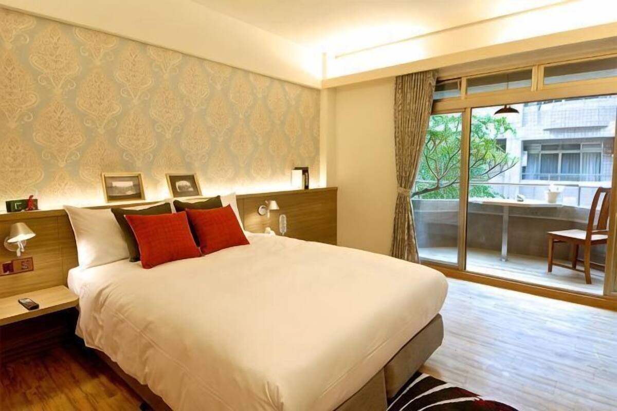 A hotel room with a large bed, bedside tables, a window with a view, and a balcony.
