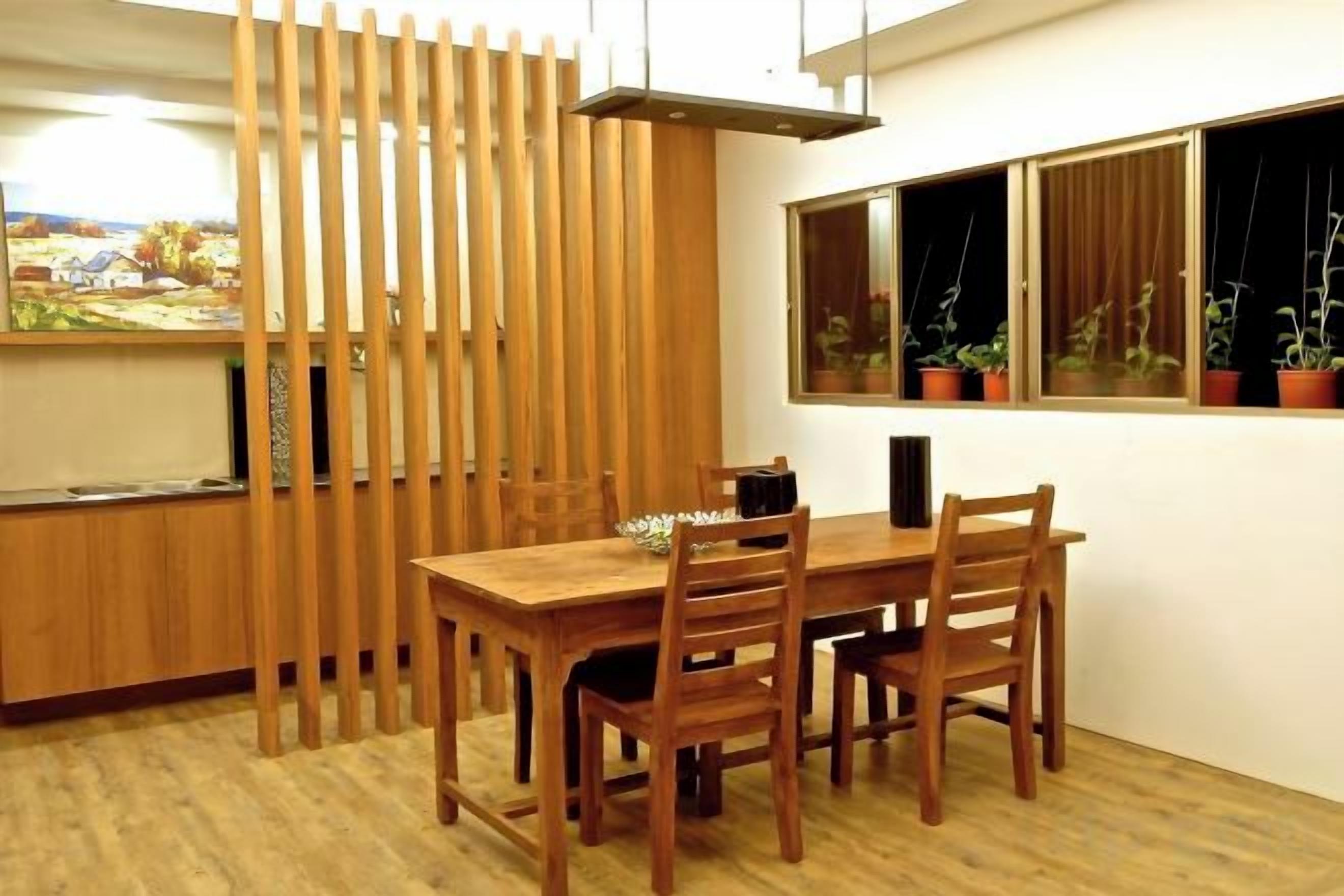 A dining area with a wooden table and chairs, a kitchen counter, and a window with potted plants.