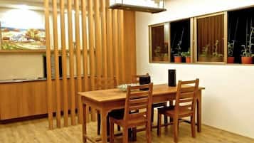 A dining area with a wooden table and chairs, a kitchen counter, and a window with potted plants.
