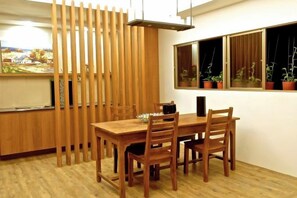 A dining area with a wooden table and chairs, a kitchen counter, and a window with potted plants.