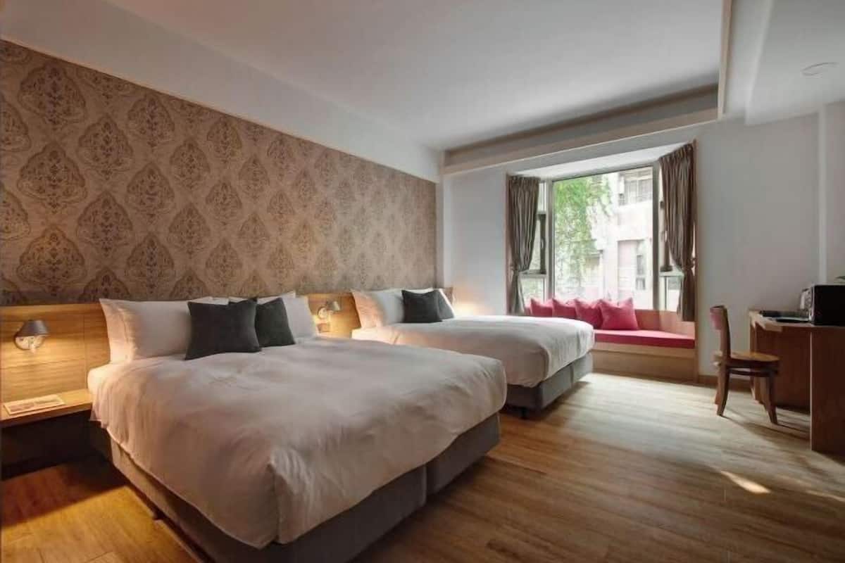A hotel room with two beds, a desk, a chair, and a window with curtains.