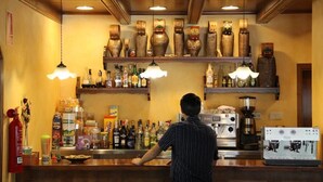 A bar area with a bartender, shelves of bottles, and a coffee machine. - Hotel El Rantiner (La Vall de Boi)