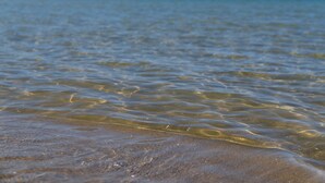 Una playa con aguas claras y poco profundas y montañas a lo lejos.