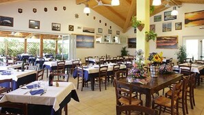 Un amplio comedor con varias mesas y sillas, vigas de madera en el techo y distintas imágenes enmarcadas en las paredes.