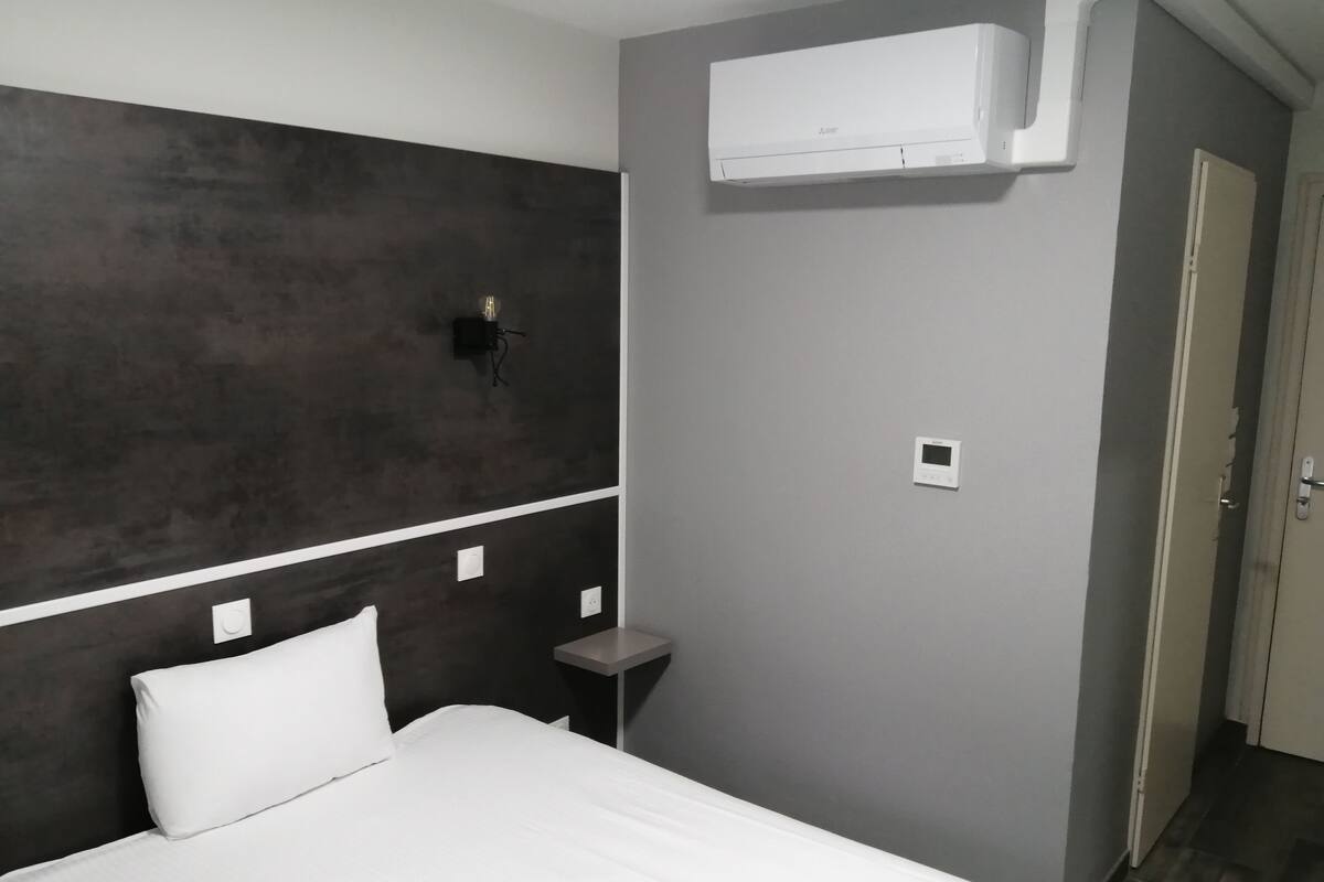 Une chambre d’hôtel avec un lit, une table de chevet, un climatiseur fixé au mur et une porte.