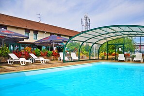 A swimming pool with lounge chairs and umbrellas, surrounded by a covered area with a glass roof. - Relais Arc en Ciel Hôtel (Wittenheim)