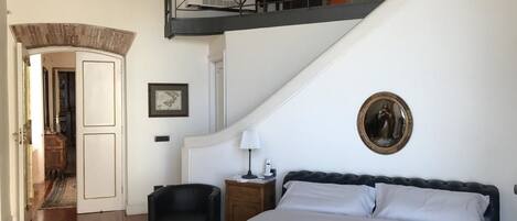 Une chambre à coucher avec un grand lit, une table de chevet, une chaise et un escalier menant à un étage supérieur.