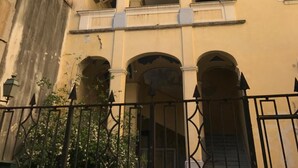 Um edifício de vários andares com fachada bege, várias varandas com caixas de flores e uma entrada em arco de pedra.