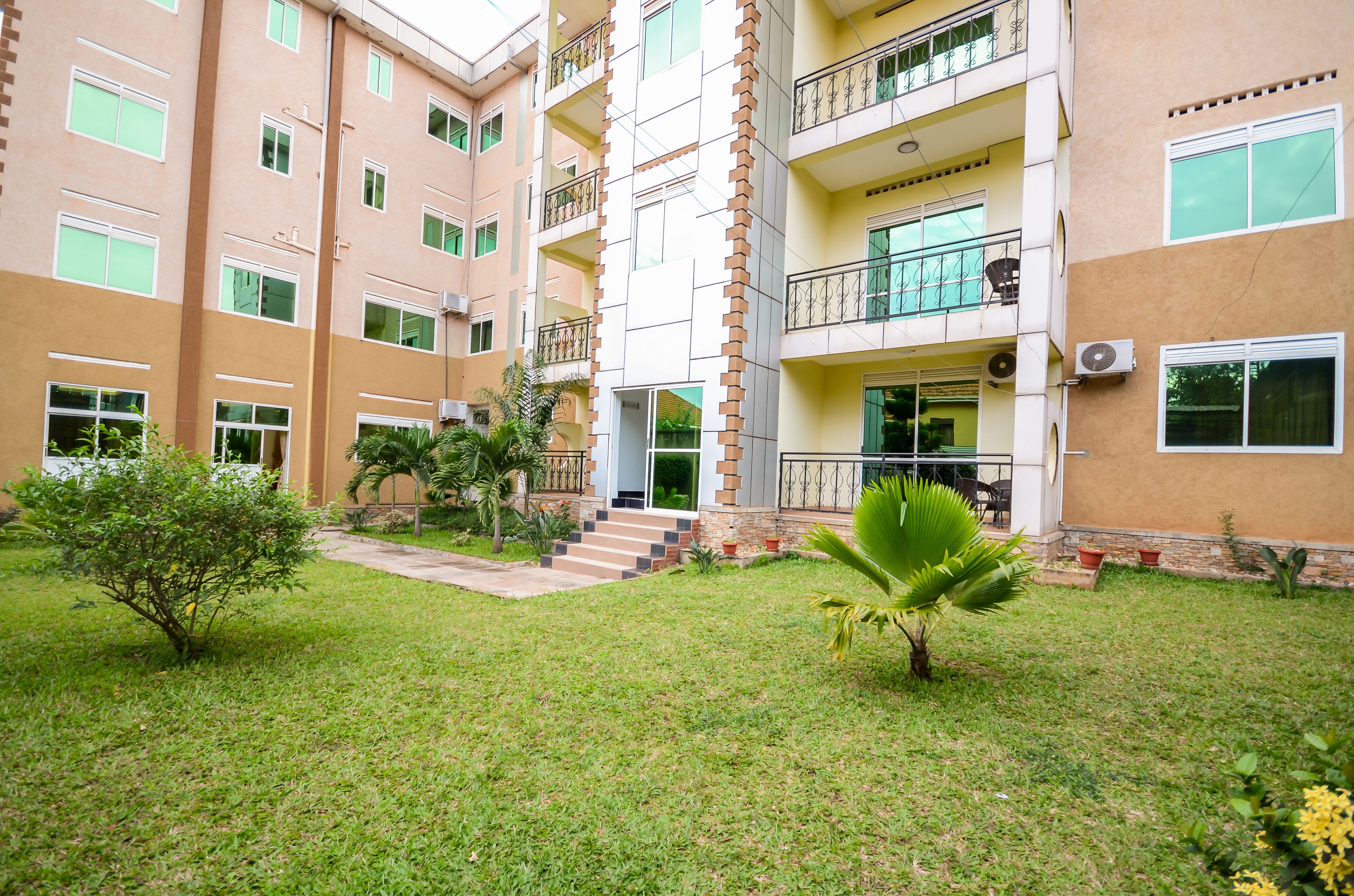 A multi-story residential building with a well-maintained lawn and small trees.