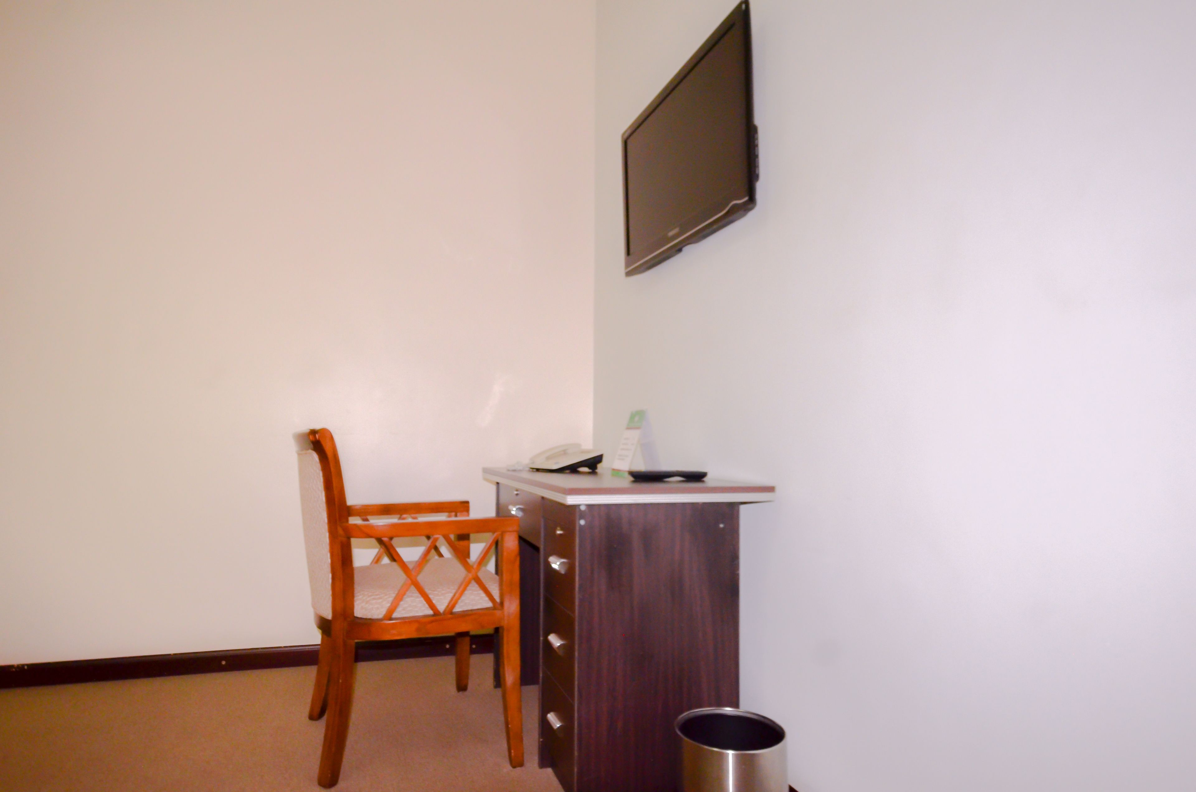 A small room with a wooden chair, a desk with a telephone, and a trash can.