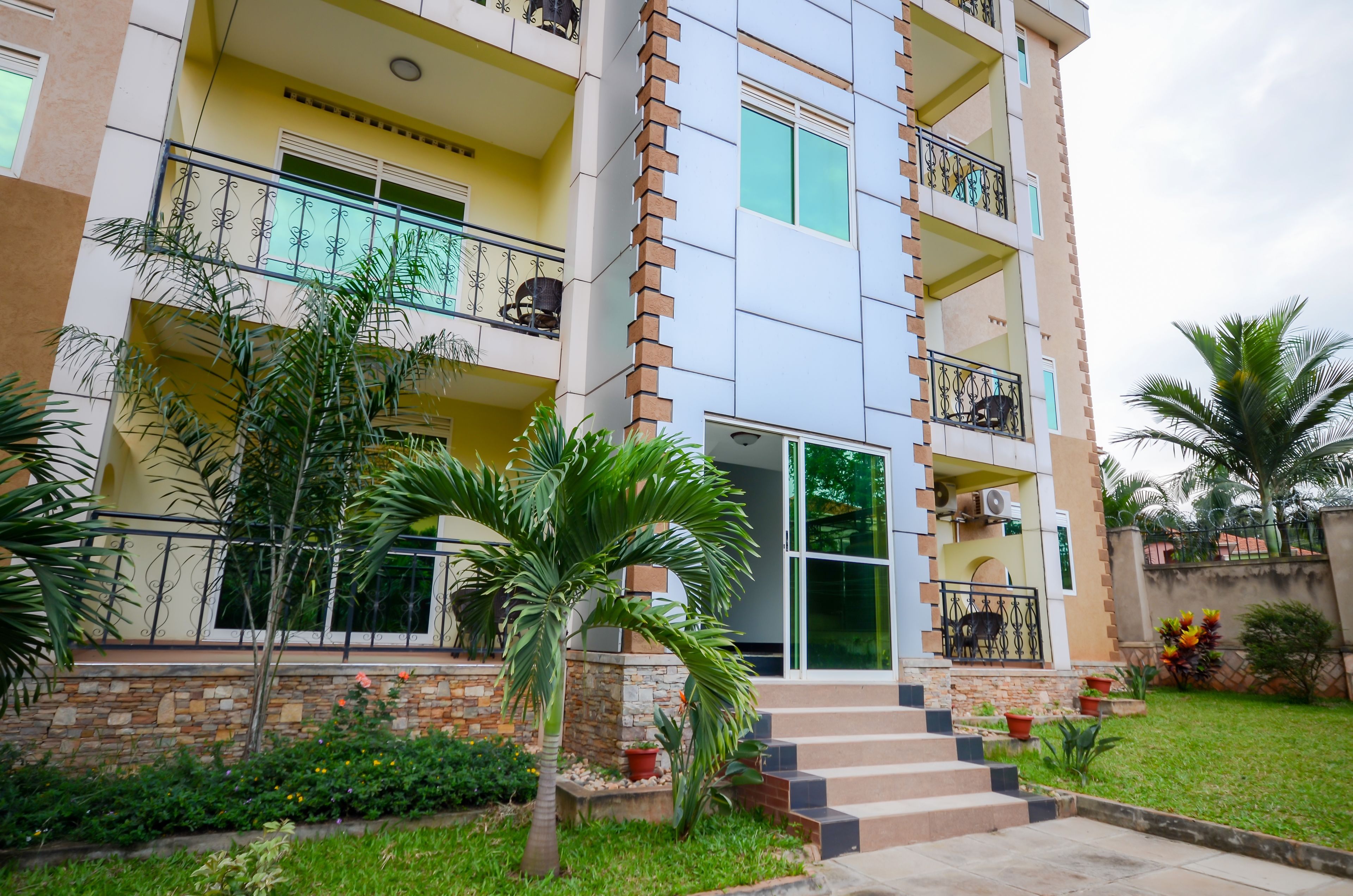 A multi-story residential building with balconies, a stone facade, and a well-maintained garden.