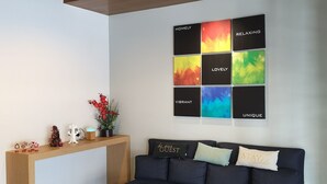 A modern living room with a dark blue sofa, a wooden console table, and a colorful abstract wall art piece. - Qlio Hotel (Kota Kinabalu)