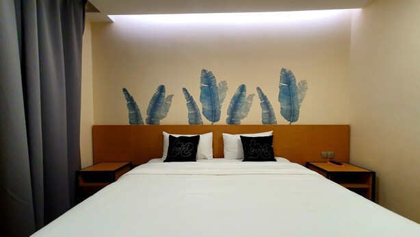 A hotel room with a large bed, two nightstands, a wall with feather artwork, and a ceiling light. - Qlio Hotel (Kota Kinabalu)