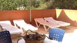 Un'area esterna con tavoli rotondi e sedie blu, un cesto di vimini con piante e un pavimento piastrellato.