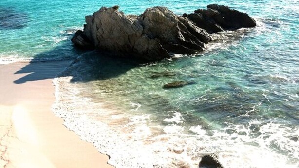 Una spiaggia con acque turchesi cristalline e un promontorio roccioso.