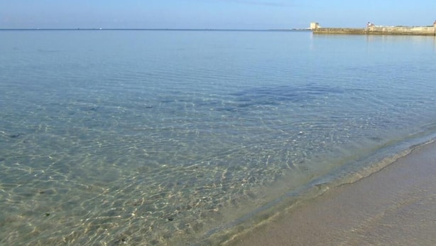 Una playa despejada con aguas tranquilas y una costa lejana.