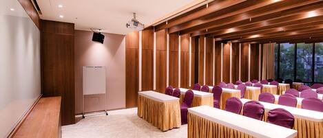 A conference room with rows of tables and chairs, a whiteboard, and a projector.