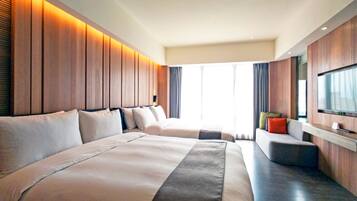 A modern hotel room with two large beds, a seating area, and a television mounted on the wall.