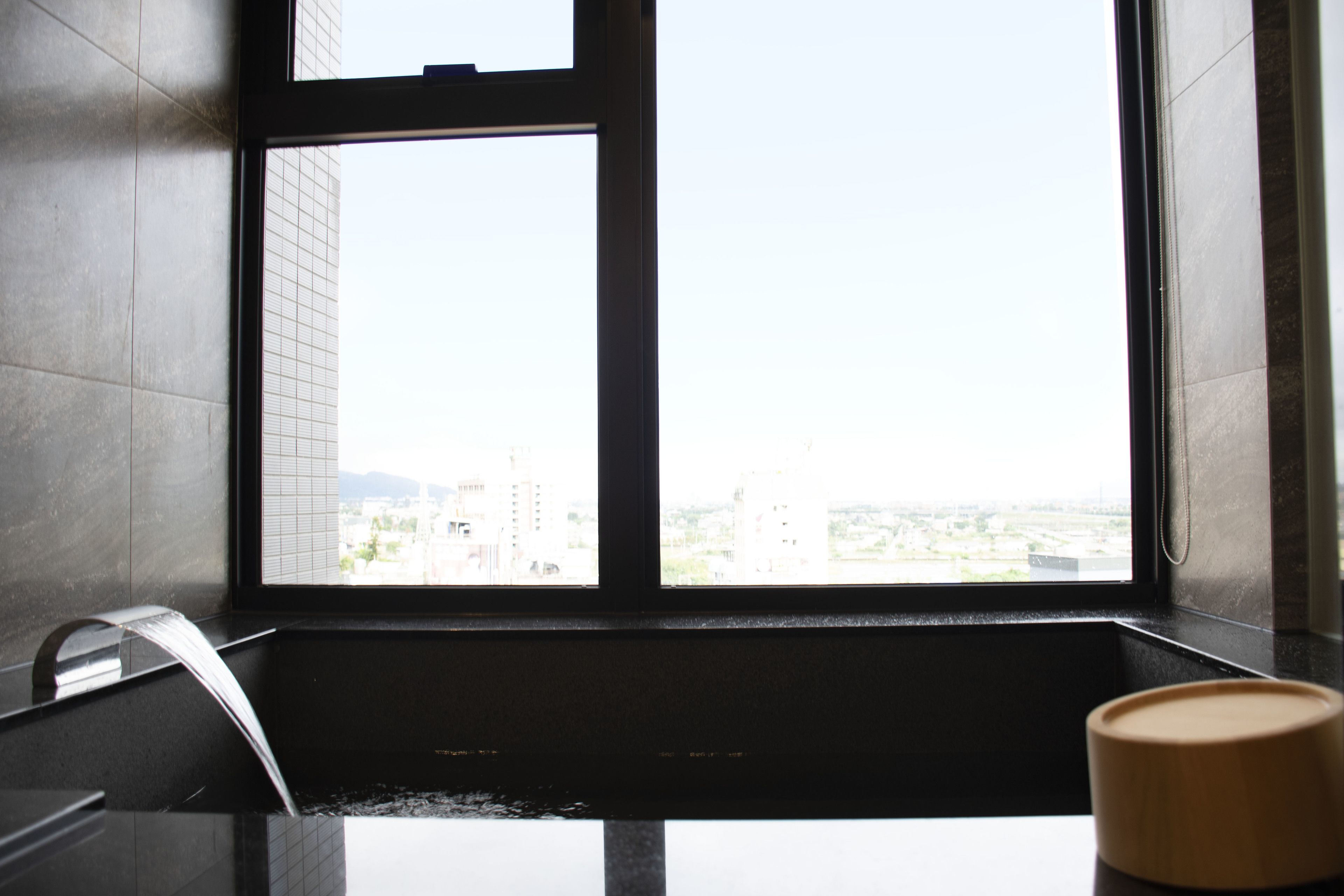Un baño con bañera, una ventana que da a edificios y un objeto de madera en la encimera.