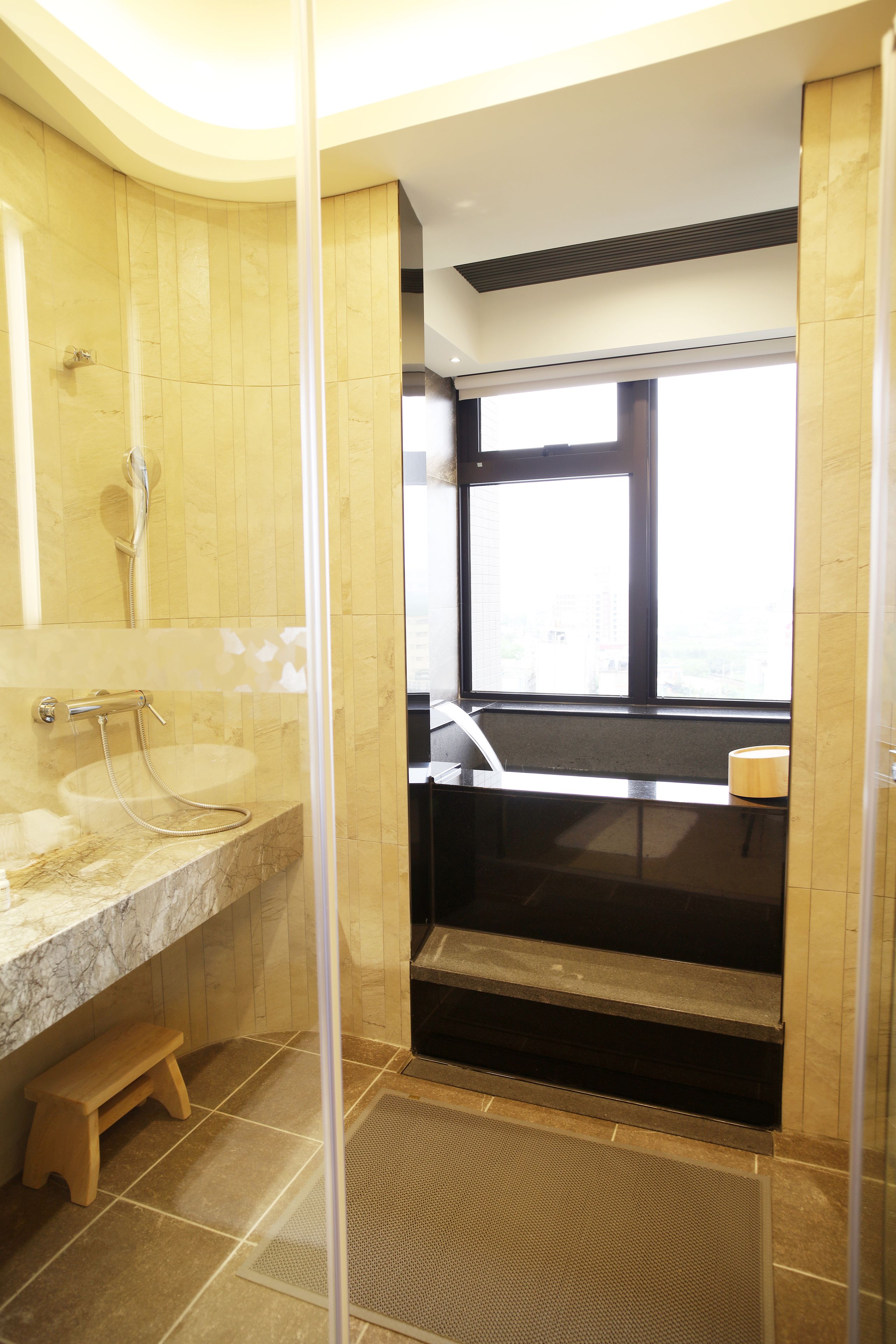A bathroom with a marble sink, a shower enclosure, and a view of the city through a window.