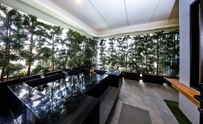 A modern indoor pool area with a glass floor, surrounded by lush greenery and a high ceiling. - Yamagata Kaku Hotel & Spa (Jiaoxi)