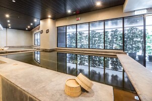 Una piscina interior moderna con paredes de vidrio transparente, un banco de madera y vistas a árboles.