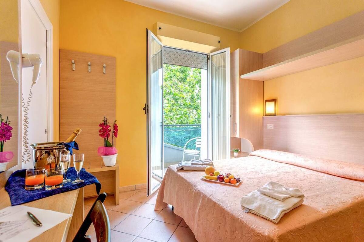 A hotel room with a bed, a table with breakfast items, a hairdryer, and a balcony with a chair.