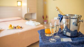Una habitación de hotel con una cama, una mesa con frutas y bebidas, y un cubo para champán.