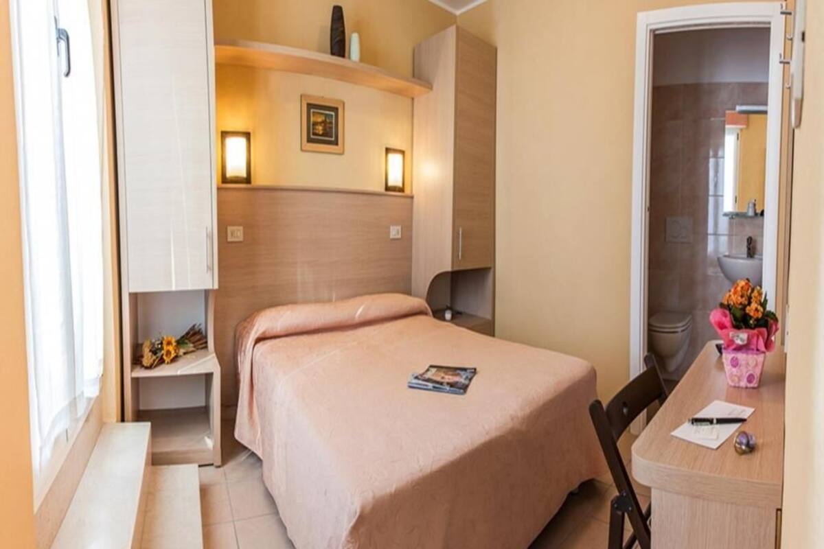 A neatly arranged bedroom with a bed, bedside tables, a desk, and a chair.