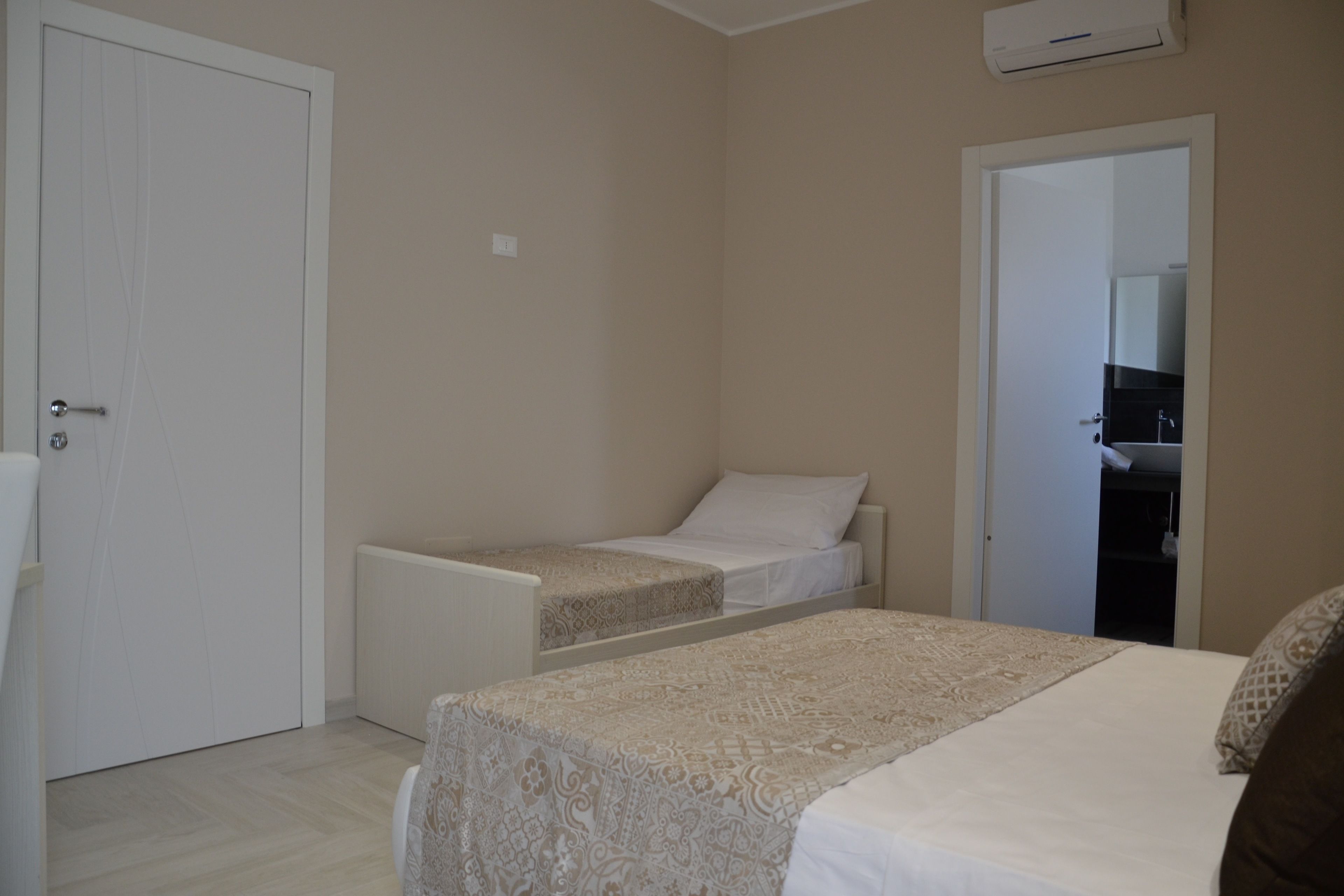 A bedroom with two beds, a white door, and a small bathroom visible through an open door.