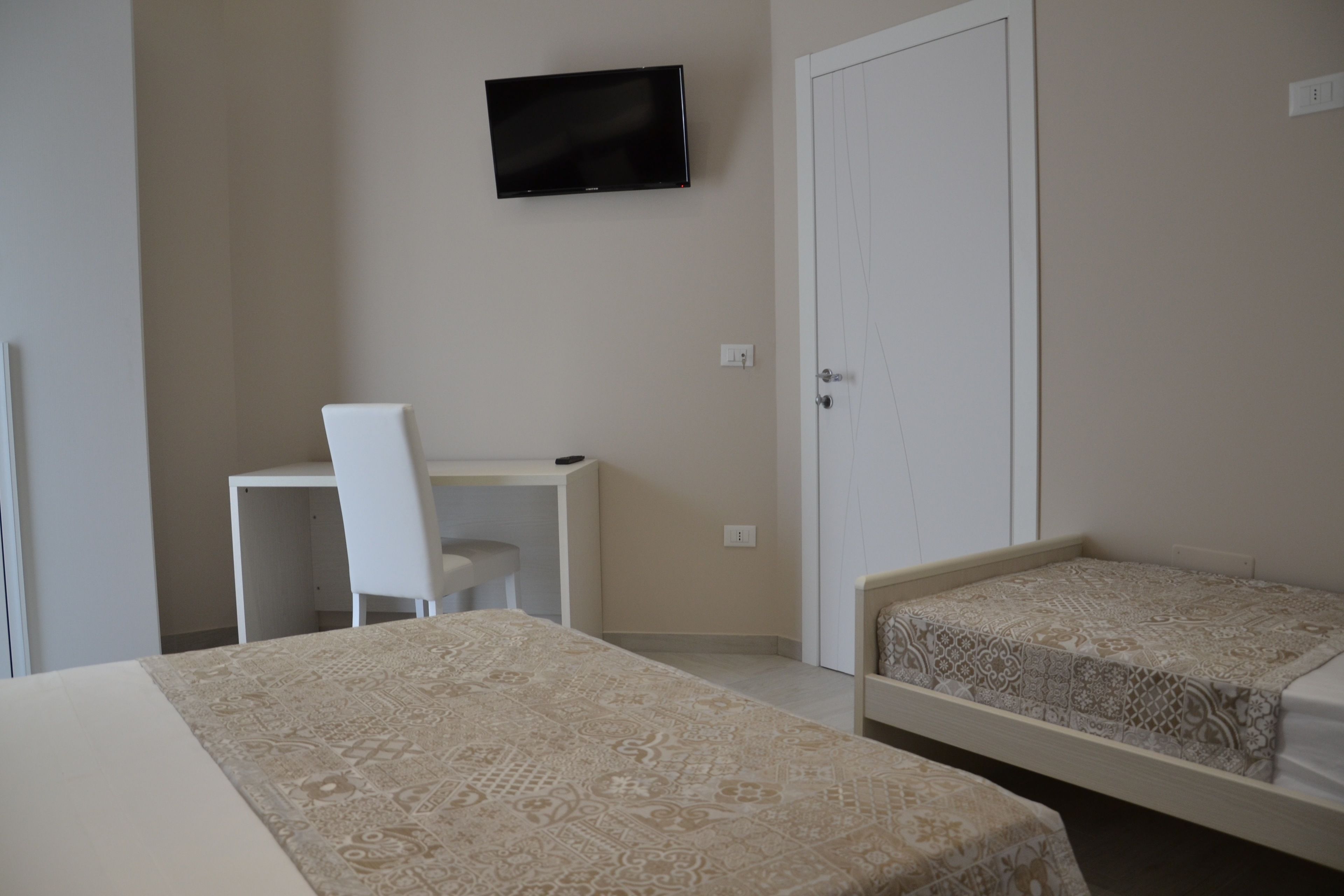 A bedroom with two beds, a desk, a chair, a television, and a wardrobe.