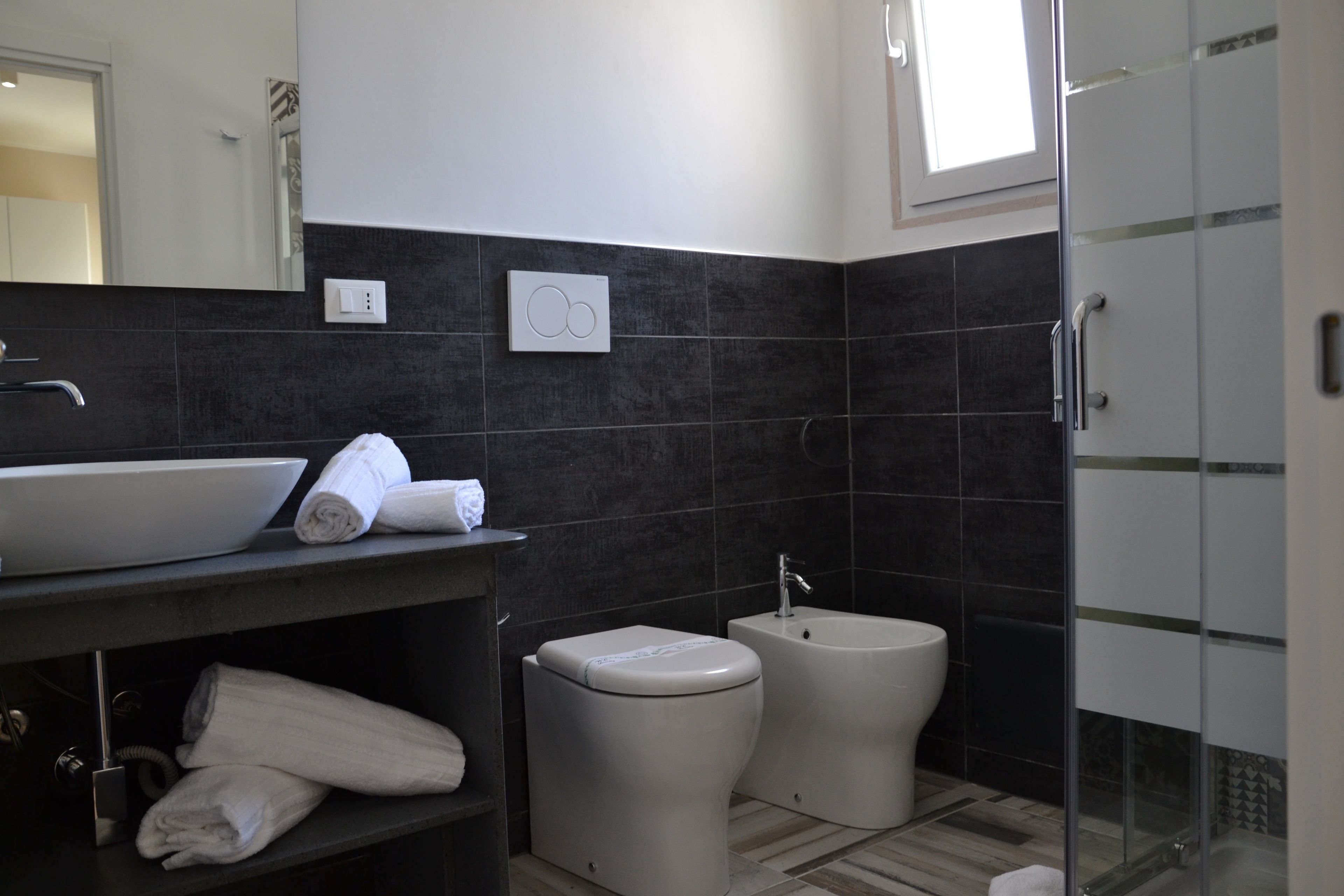 A modern bathroom with a large sink, two toilets, and a glass shower enclosure.
