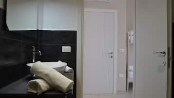 A modern bathroom with a dark tiled wall, a white sink, and a towel on the counter.