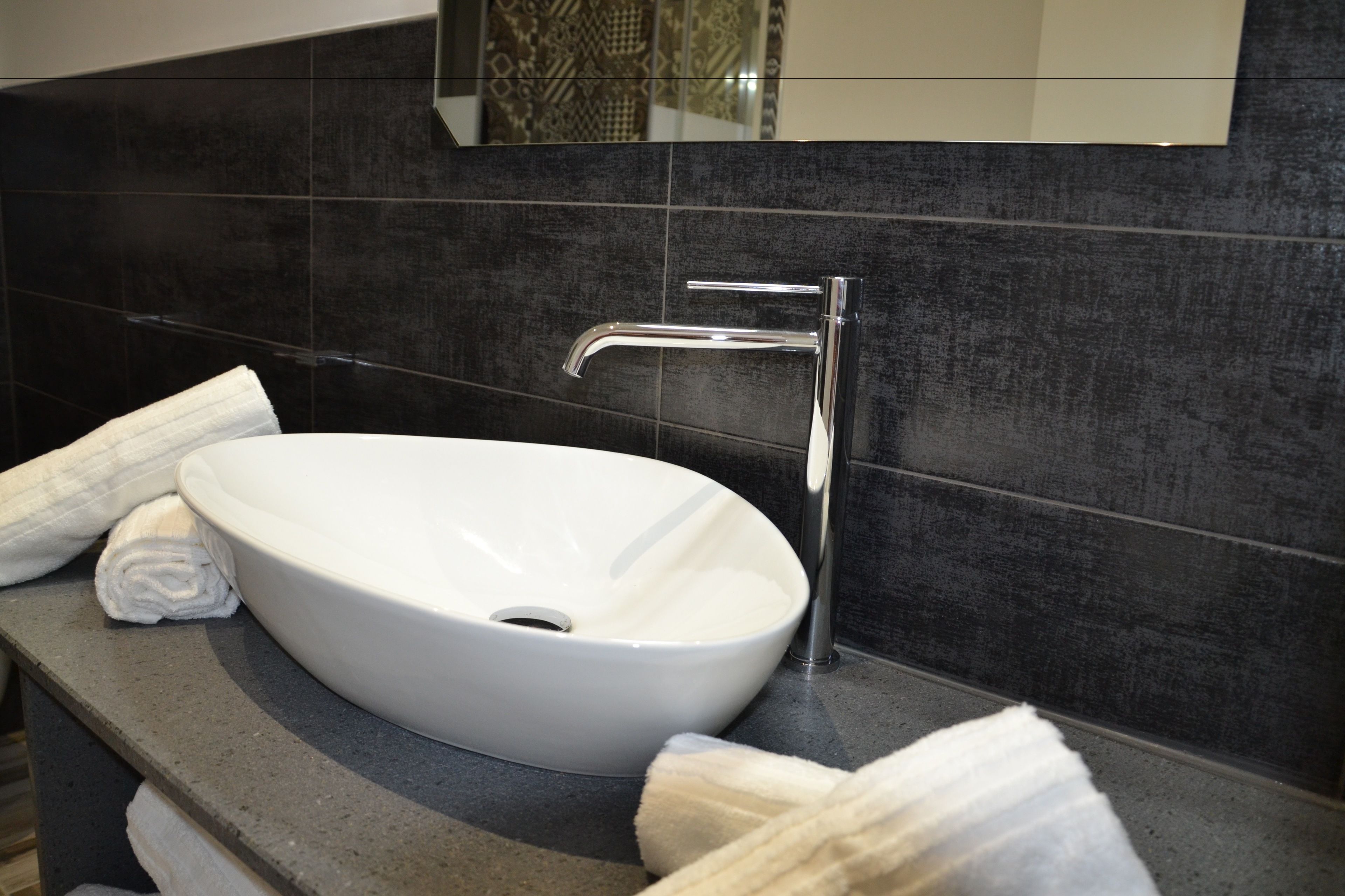 Une salle de bain moderne avec un lavabo blanc, des murs recouverts de carreaux foncés et un miroir au-dessus du lavabo.