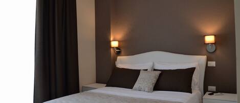 Una habitación de hotel moderna con una cama grande, dos lámparas de noche, una mesita de noche y una ventana con cortinas.