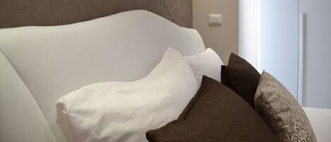 A modern bedroom with a white headboard, a patterned wall, and a white wardrobe.