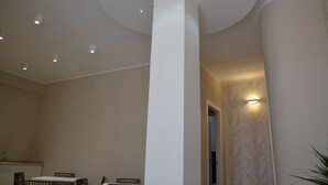 Un interior moderno con techo alto, iluminación empotrada, una columna central y un comedor con sillas y mesa.