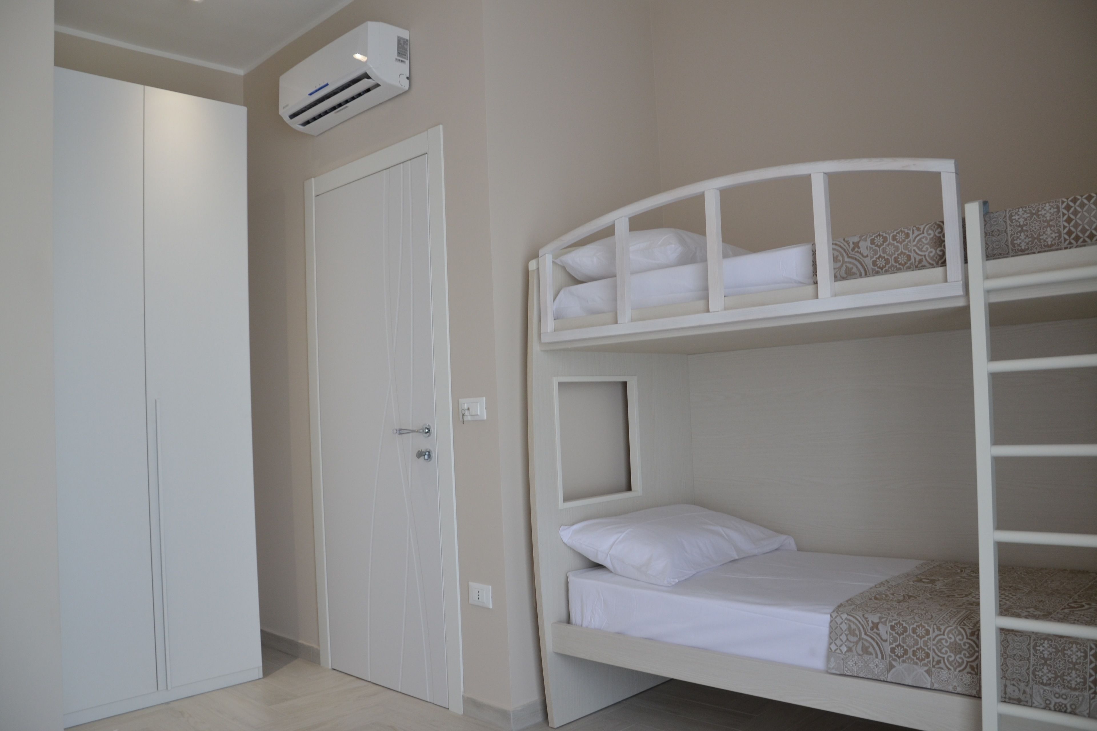 A bunk bed room with a white wardrobe and an air conditioning unit.