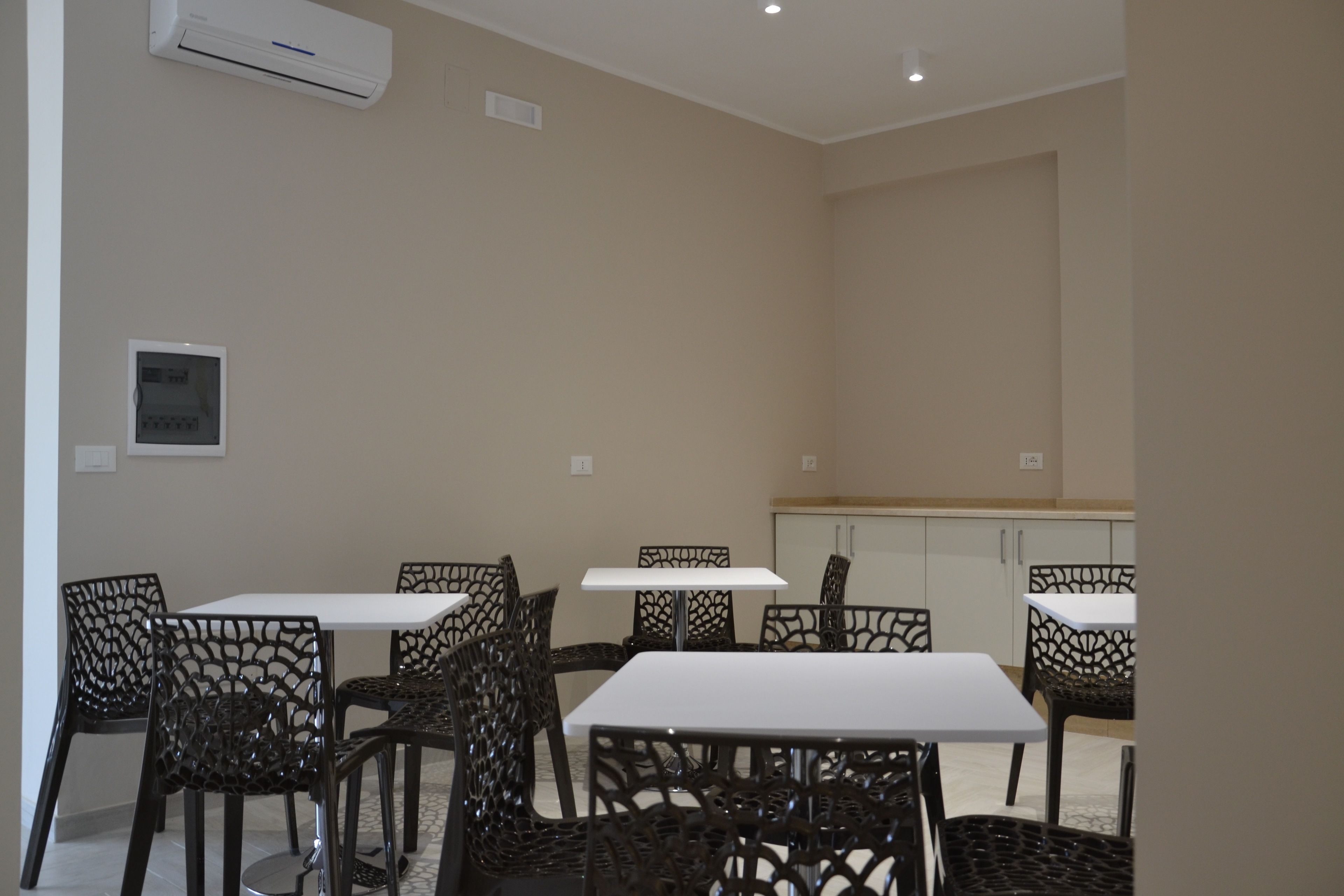 Un espace repas avec six tables et chaises, un appareil de climatisation et une cuisine en arrière-plan.