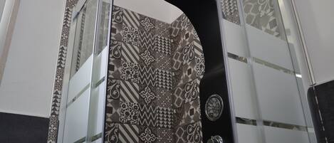 A shower with a black curved showerhead and a patterned tile wall.