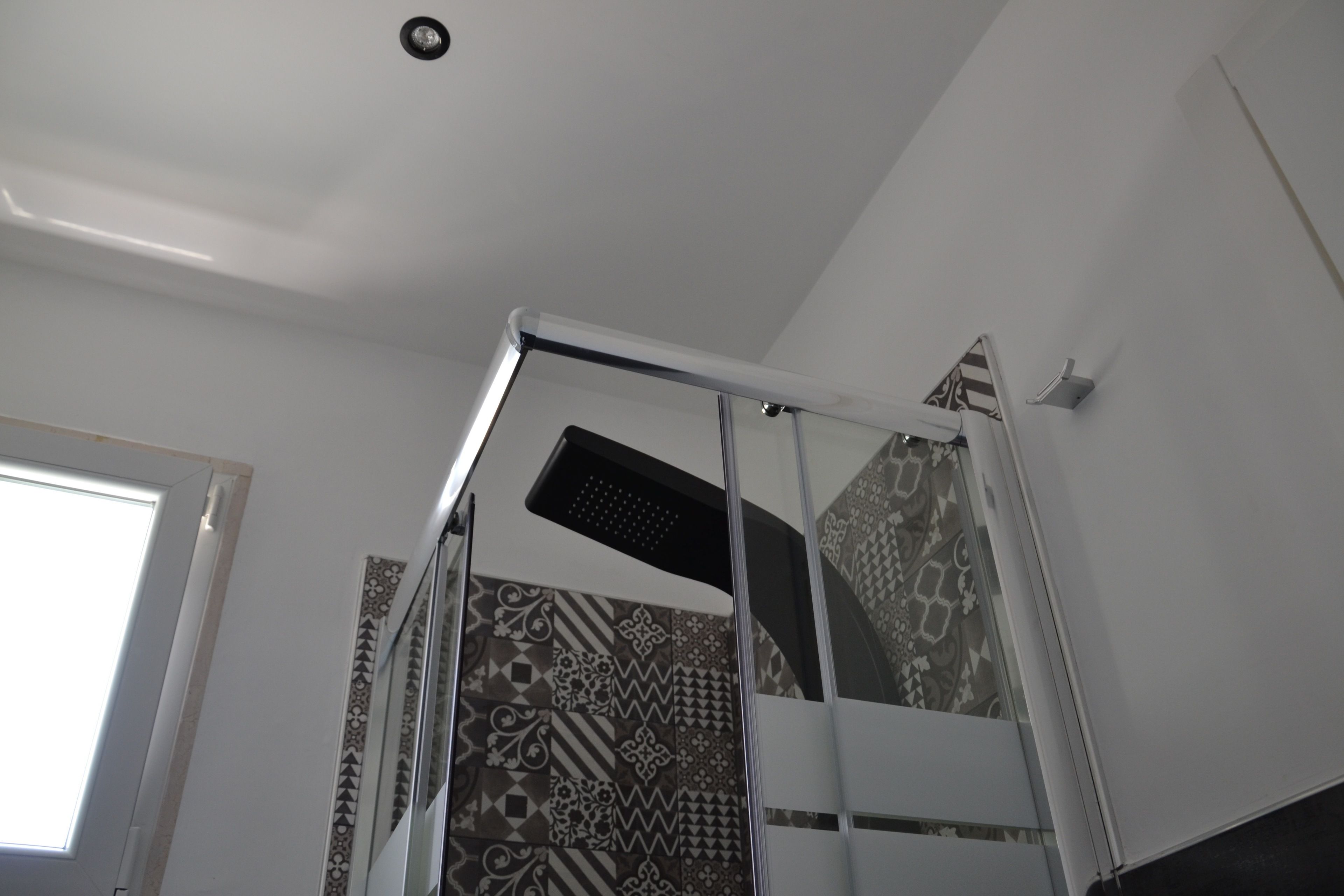 A shower area with a glass door, patterned tiles, and a ceiling light fixture.