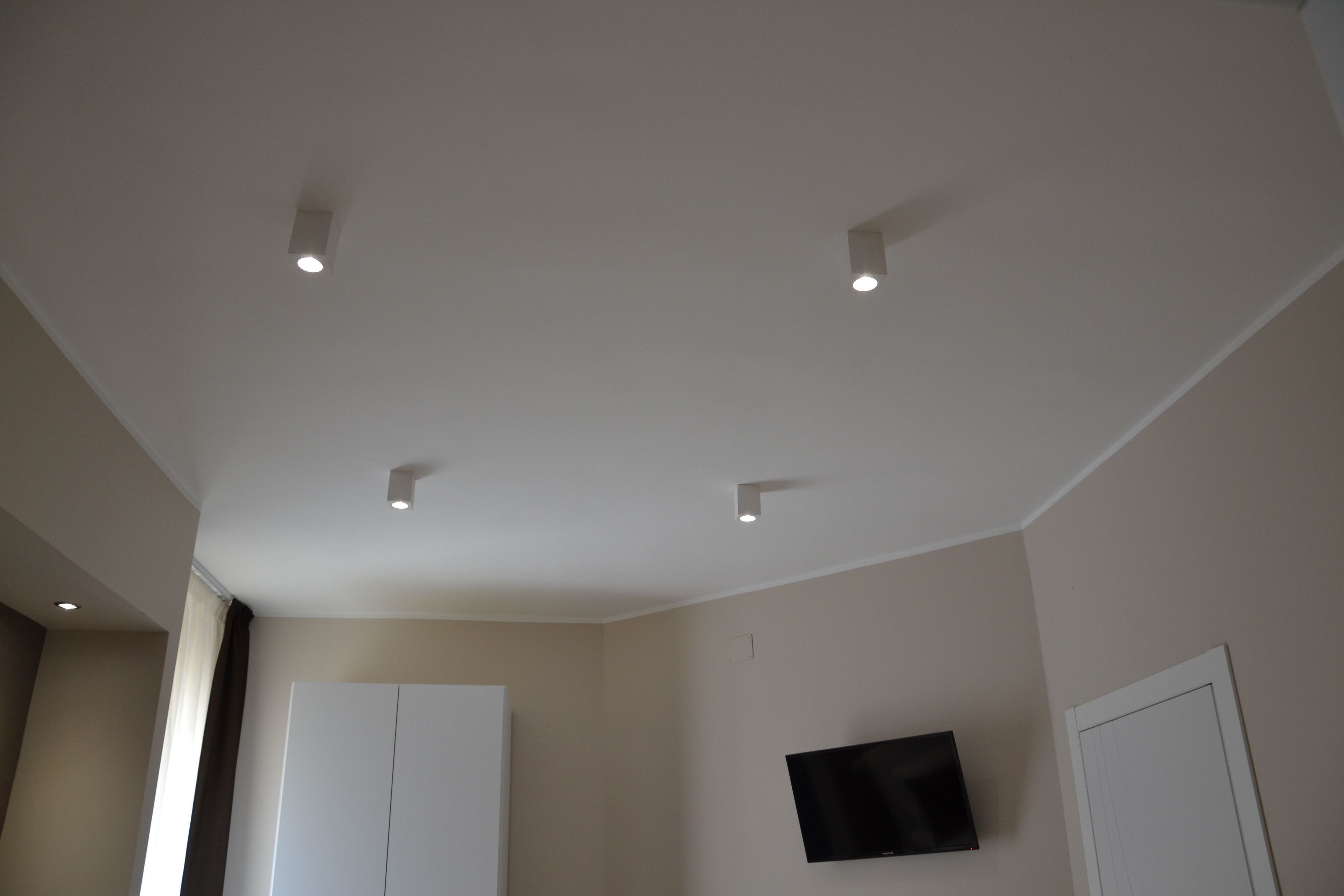 Una habitación con televisor de pantalla plana en la pared, luces empotradas en el techo y un armario blanco grande.